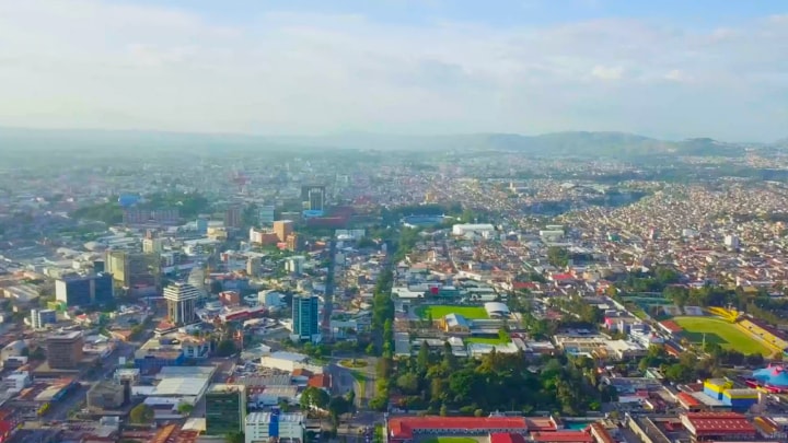 A vibrant cityscape with numerous buildings adjacent to a spacious green field, showcasing urban and natural elements.