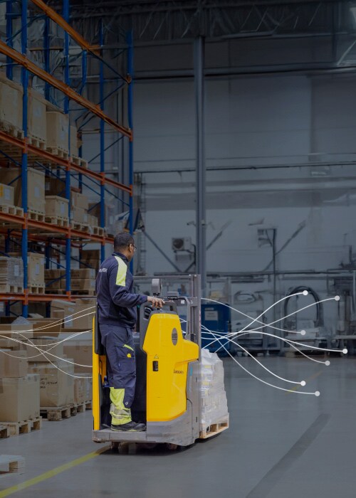 A worker moves cargo in a smart warehouse, highlighted by data flow lines representing digital logistics.