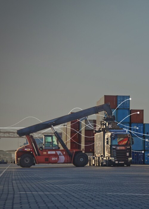 A reach stacker loads a container onto a truck at a shipping yard.