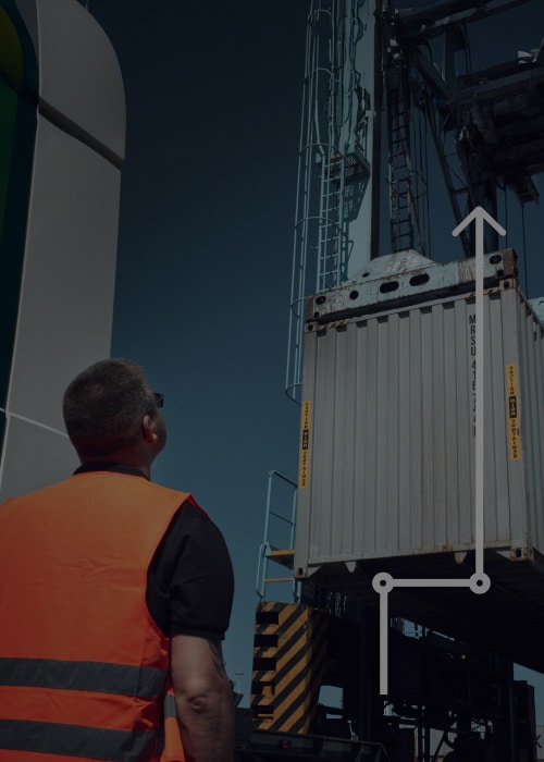 Trabalhador observando contêiner içado por guindaste