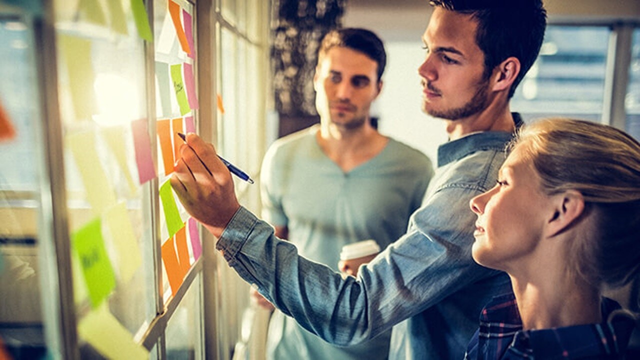 Três funcionários da Maersk em um escritório; um deles escreve em uma nota adesiva.