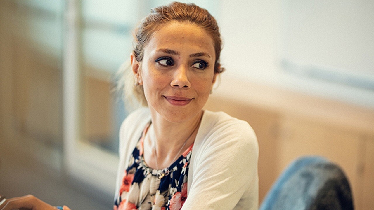 A female UX design employee seated at her workstation is smiling and looking to her left.