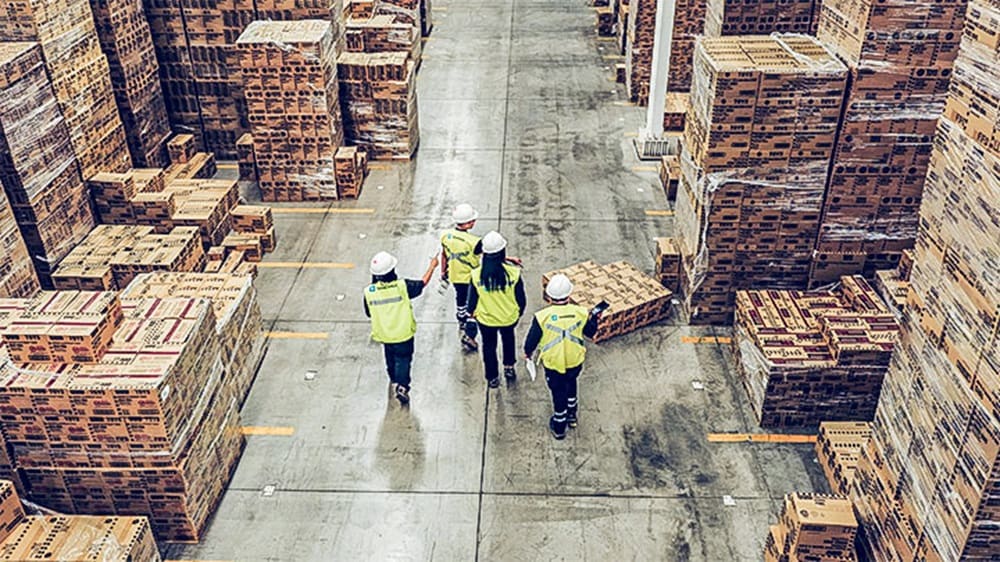 Warehouse team walking through a large storage facility with stacked pallets and boxes