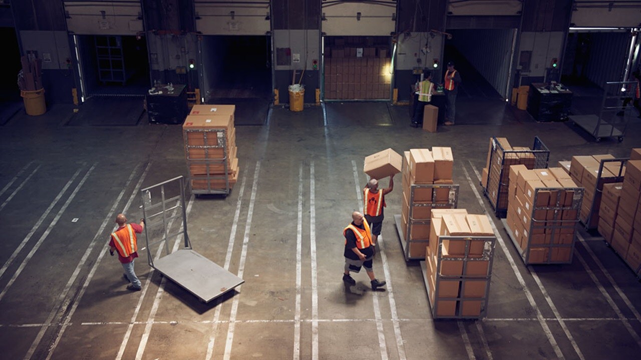 Arial view of the loading bay in a warehouse with workers wearing high vis vests moving boxes around on trolleys
