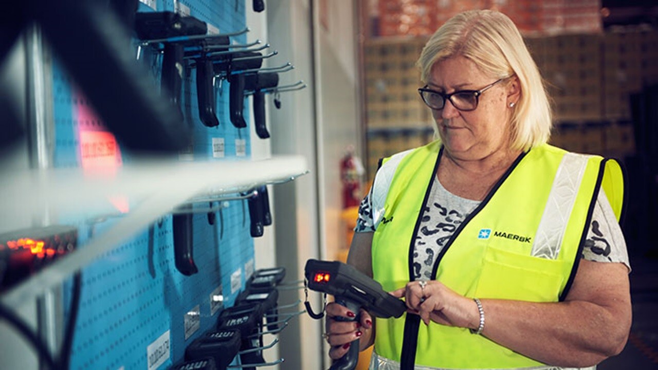 A blonde woman with glasses is wearing a hi-vis yellow vest over her t-shirt