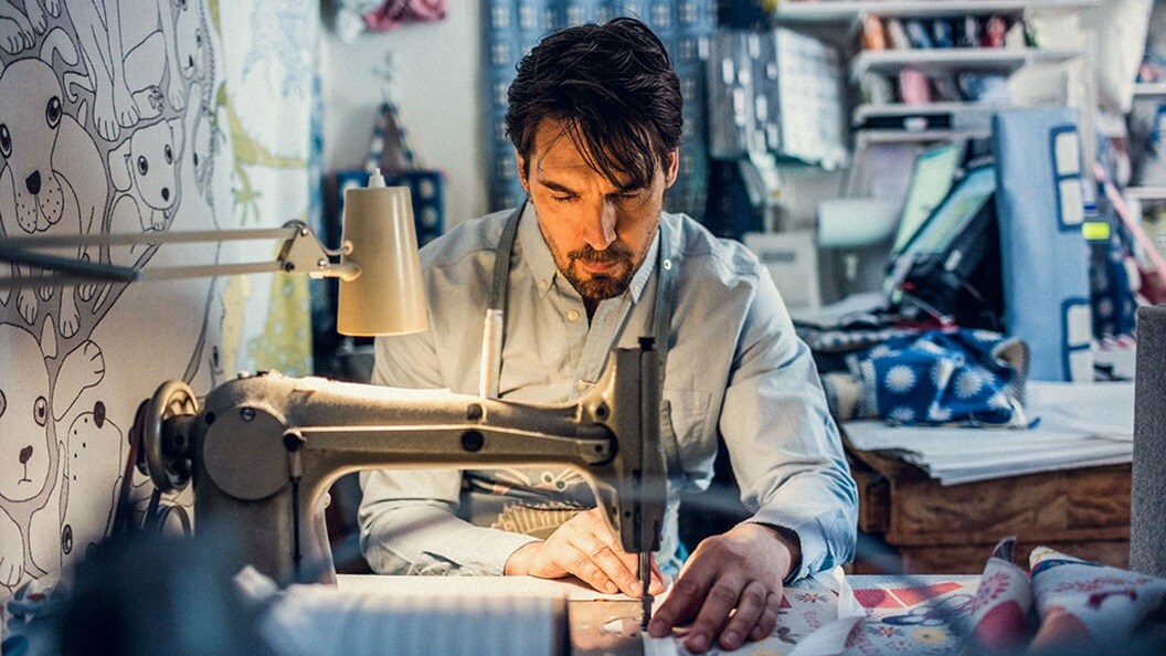 Man sitting at a sewing machine sewing together fabrics
