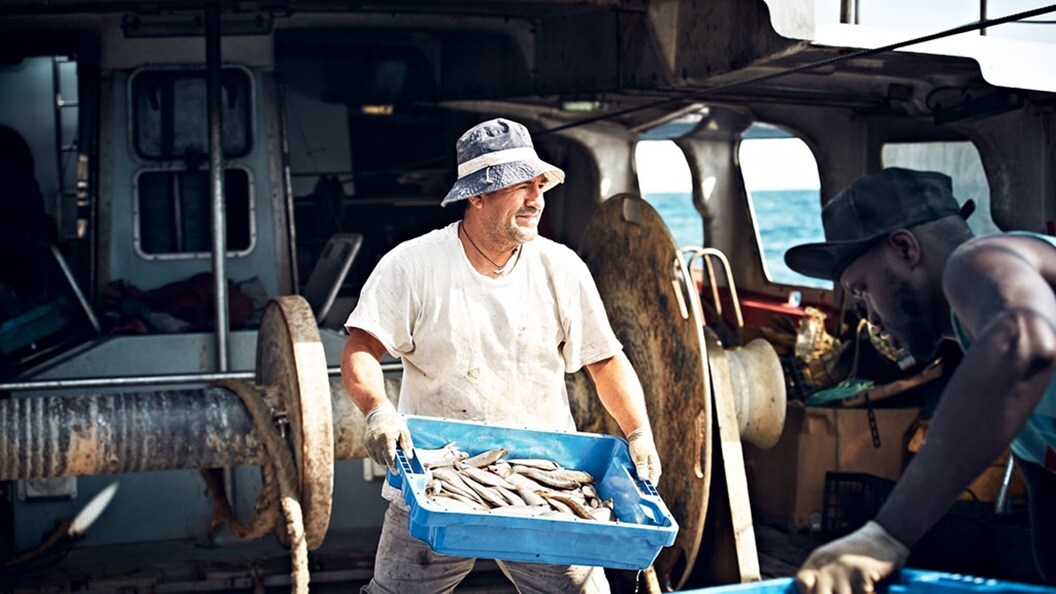 Worker carrying fish crate on a trawler