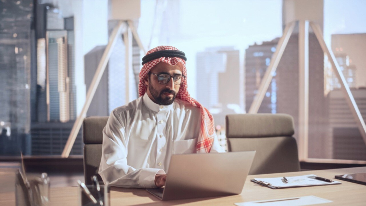Arab businessman focused on his laptop while working in a modern office setting.