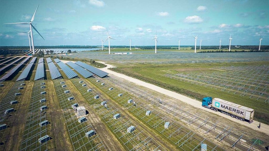 Solar panels, wind turbines, and a Maersk truck in a renewable energy farm.