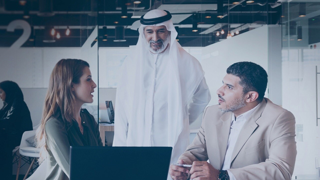Three business professionals collaborating in a modern office environment, discussing strategies and reviewing documents.