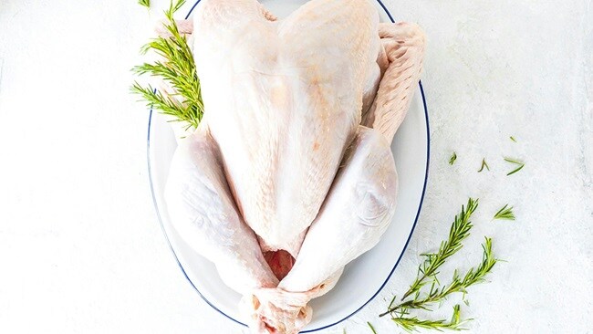 a whole chicken on a plate with a sprig of rosemary