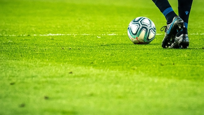 A soccer green field with a football and a pair of feet about to kick it
