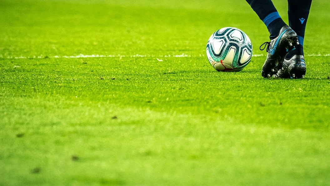 A soccer green field with a football and a pair of feet about to kick it