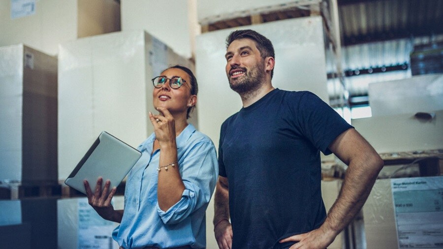  A man and woman are positioned in a warehouse filled with boxes, collaborating on logistics and storage solutions.