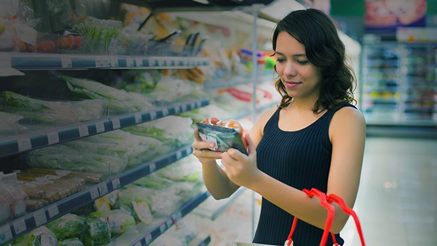 A smiling young woman holding an FMCG product in a supermarket.
