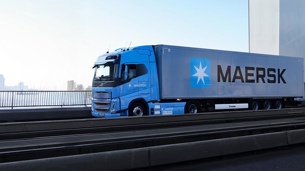 Maersk container truck driving across a modern bridge with city skyline and waterfront in the background