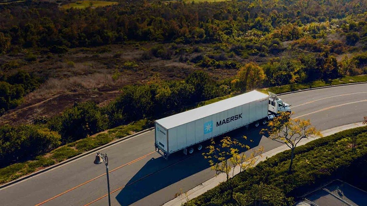 Maersk container truck driving on a curved suburban road surrounded by greenery and trees