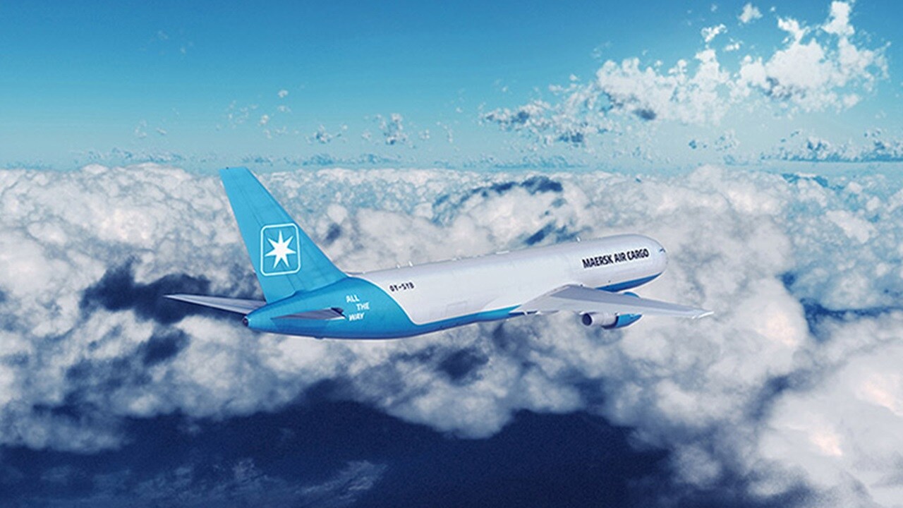 Two female professionals discussing logistics data on a laptop inside a warehouse with shelves and boxes