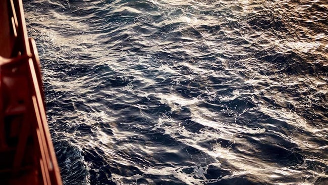 Ocean surface with sunlight reflections viewed from the side of a cargo ship.