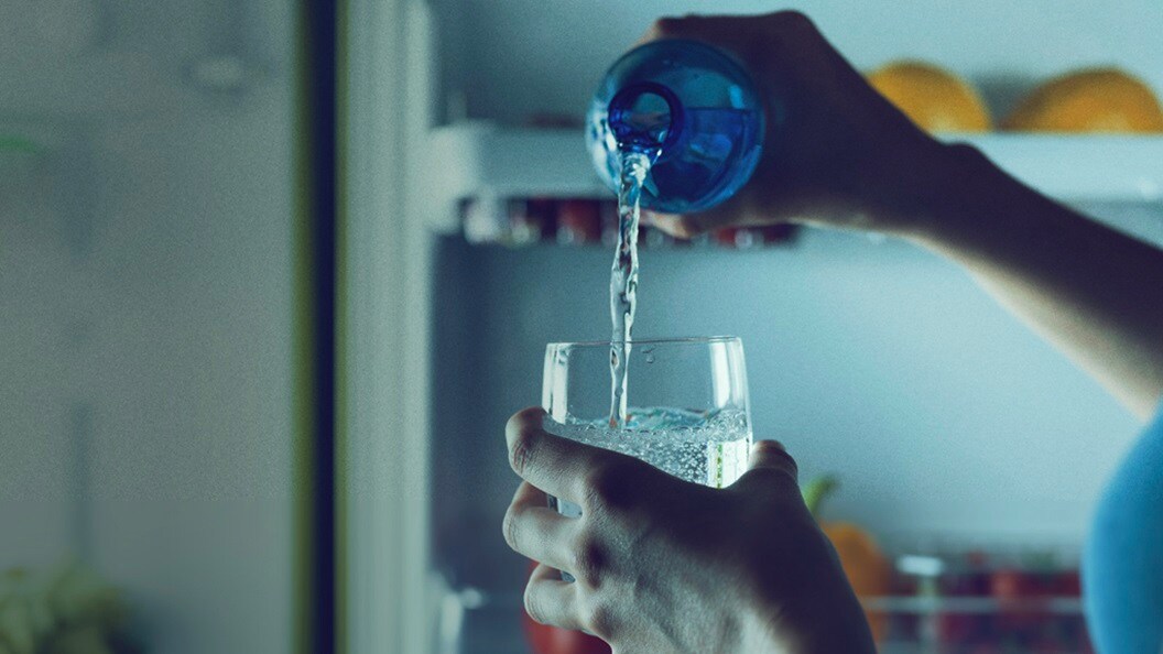 person pouring water from a blue bottle into a glass