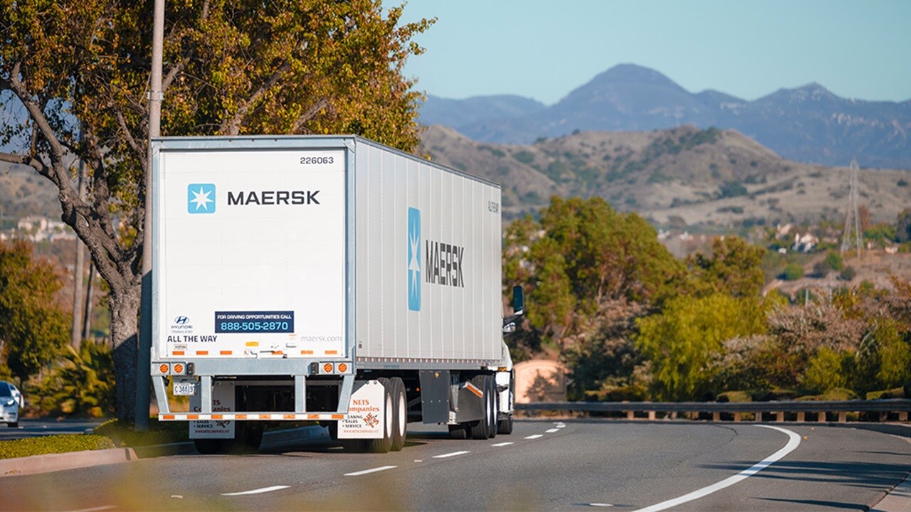 Maersk semi-trailer truck driving on a curved suburban road