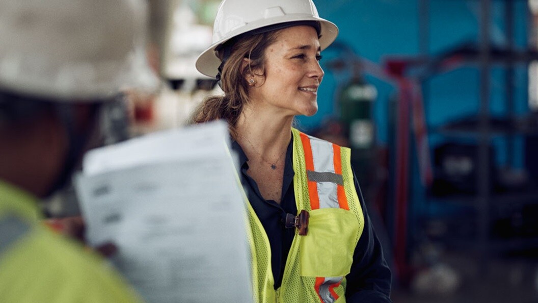 A woman and a man wearing protective clothing reviewing documents in a warehouse.