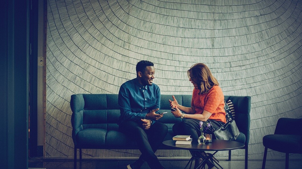 Customer supply chain management – A man and a woman, seated on a sofa, discussing in an office.