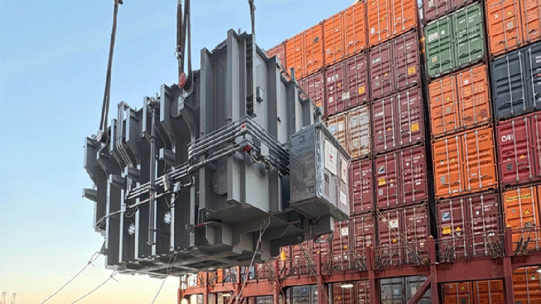Transformer being lifted in front of shipping containers
