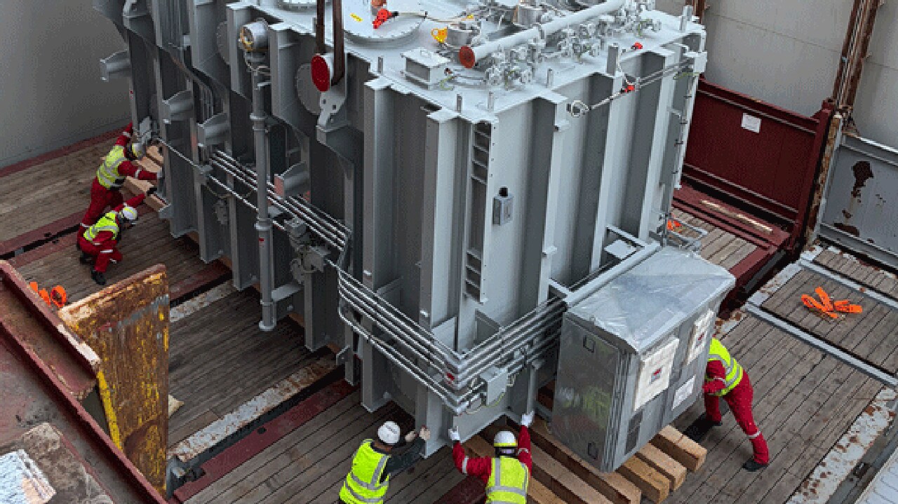 Transformer being positioned on a trailer by workers