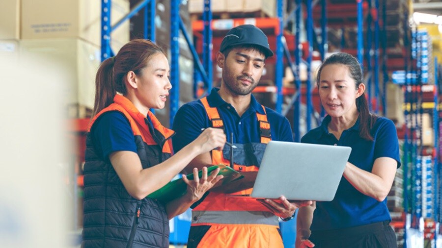 Two female and a male working on a laptop in a warehouse