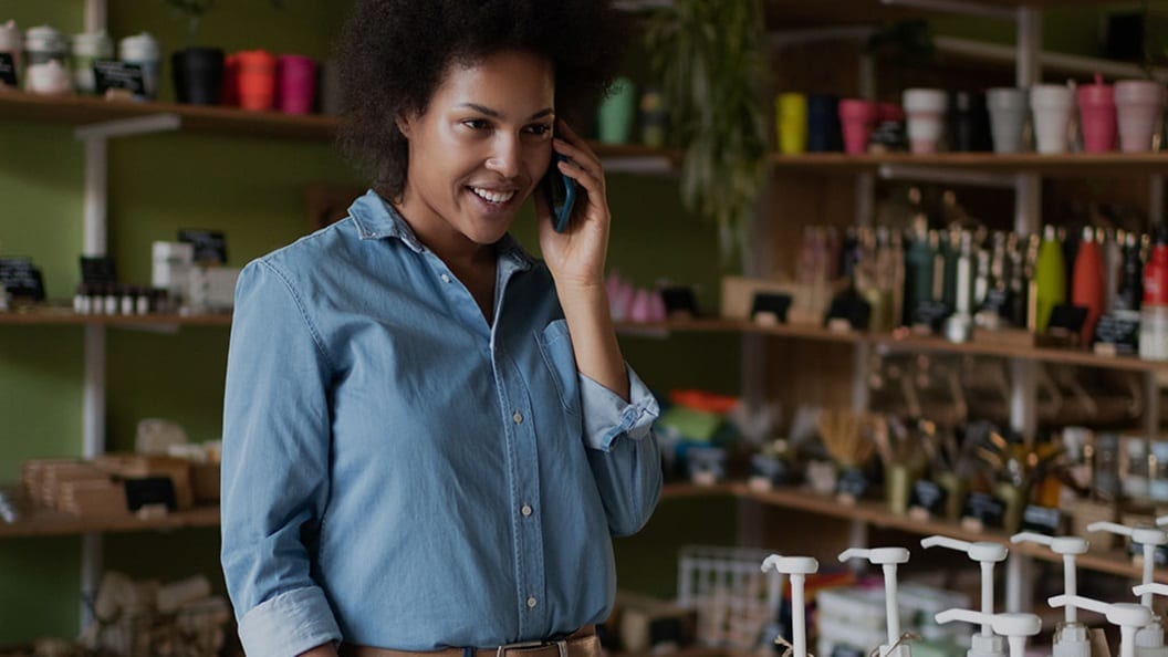 A smiling woman, talking on phone, surrounded by shelves in a supermarket.