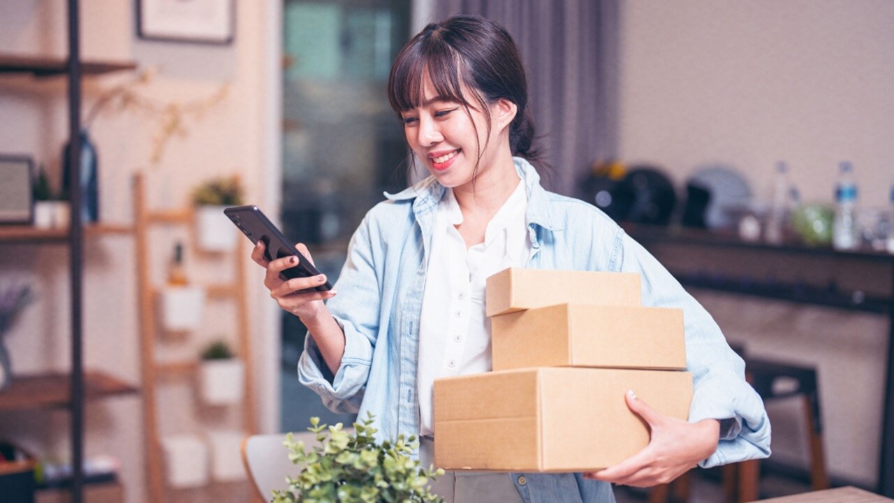 Image of a girl with boxes in one hand, seeing into her phone on the other hand