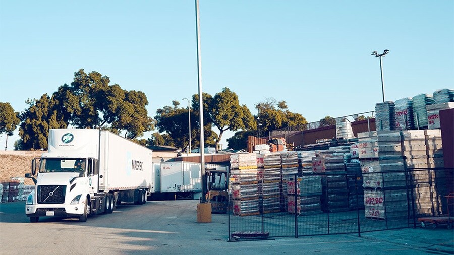 White semi-truck with trailer parked in a lot with construction materials on pallets.