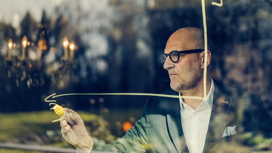 Man in a suit drawing a graph on glass.