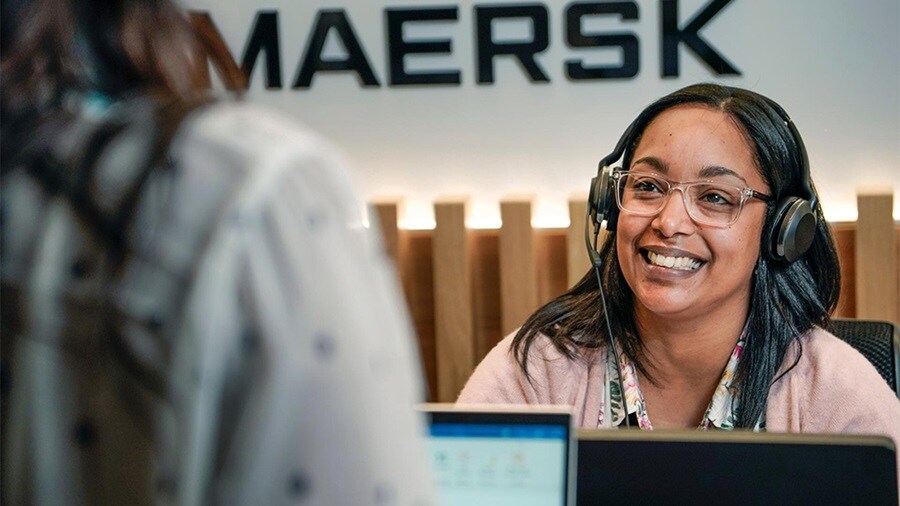 Smiling customer service representative wearing a headset, assisting a client at a Maersk service center.