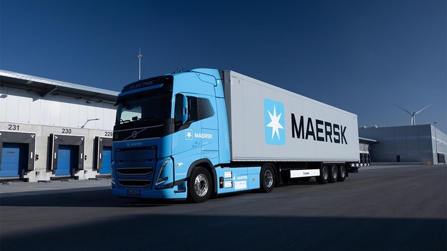 Maersk-branded electric truck parked at a logistics facility with loading docks, highlighting sustainable inland transportation.
