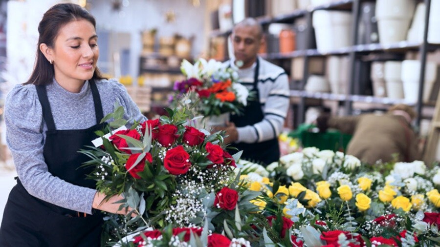 A woman holds a vibrant bouquet of flowers while standing in a colorful flower shop filled with various floral arrangements.