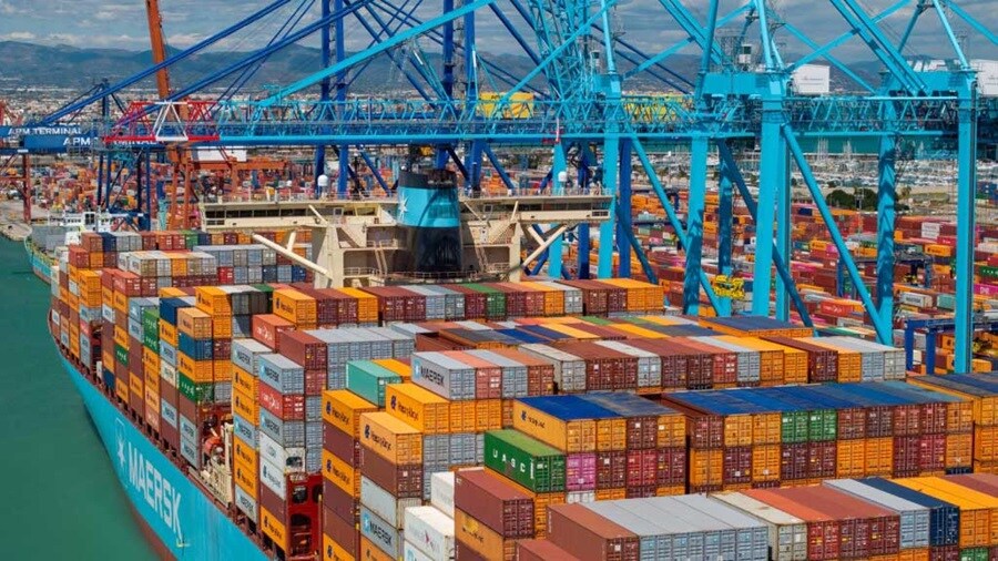 A large container ship rests at the dock, surrounded by cranes and stacks of cargo containers at the port.