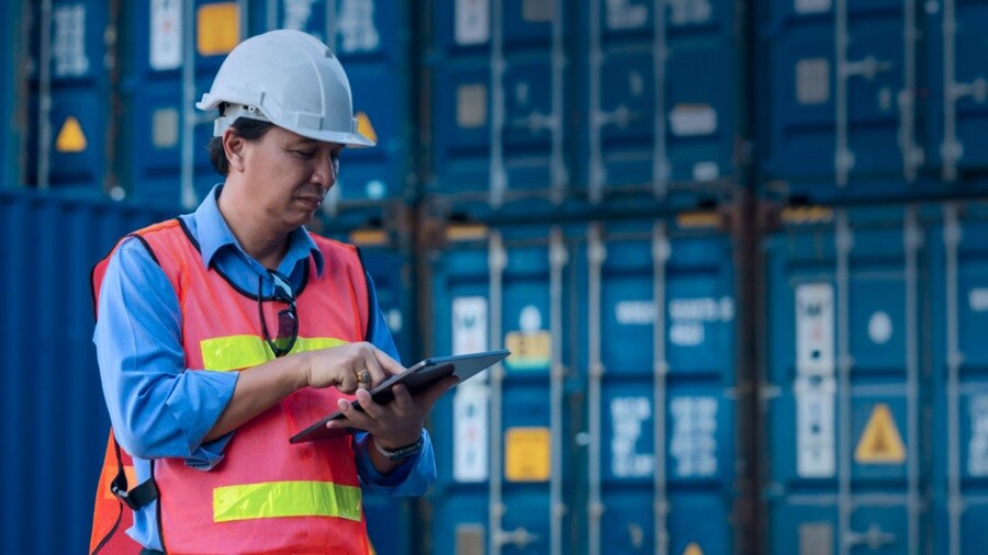 A construction worker in a hard hat and vest is holding a tablet, engaged in a task on a job site.