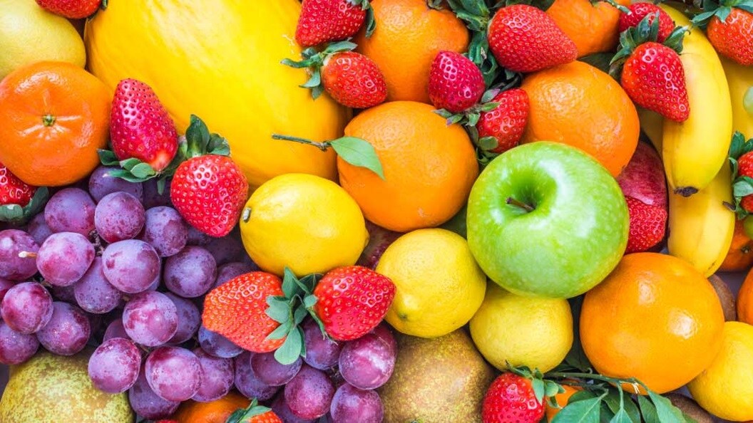 A man harvesting ripe cherries from a tree, reaching up to gather the fruit with a focused expression.