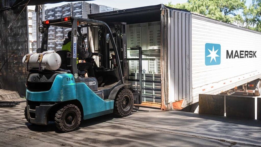 A forklift is lifting a container and placing it onto the bed of a truck in a loading area.