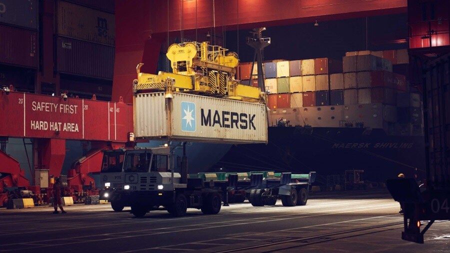 Maersk container being loaded onto a truck at a port terminal at night.