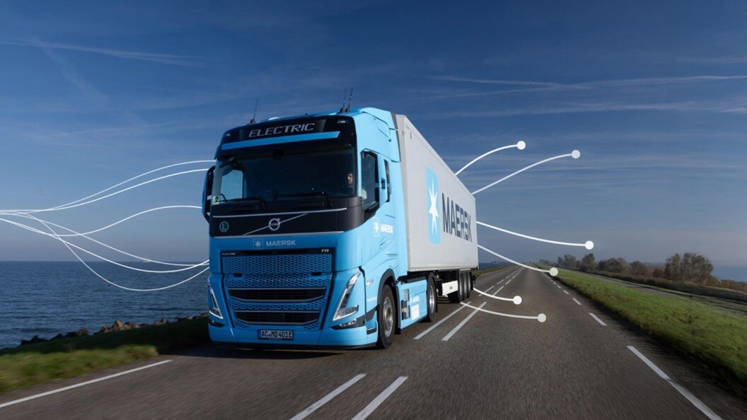 Maersk electric truck driving along a coastal highway under a clear blue sky.