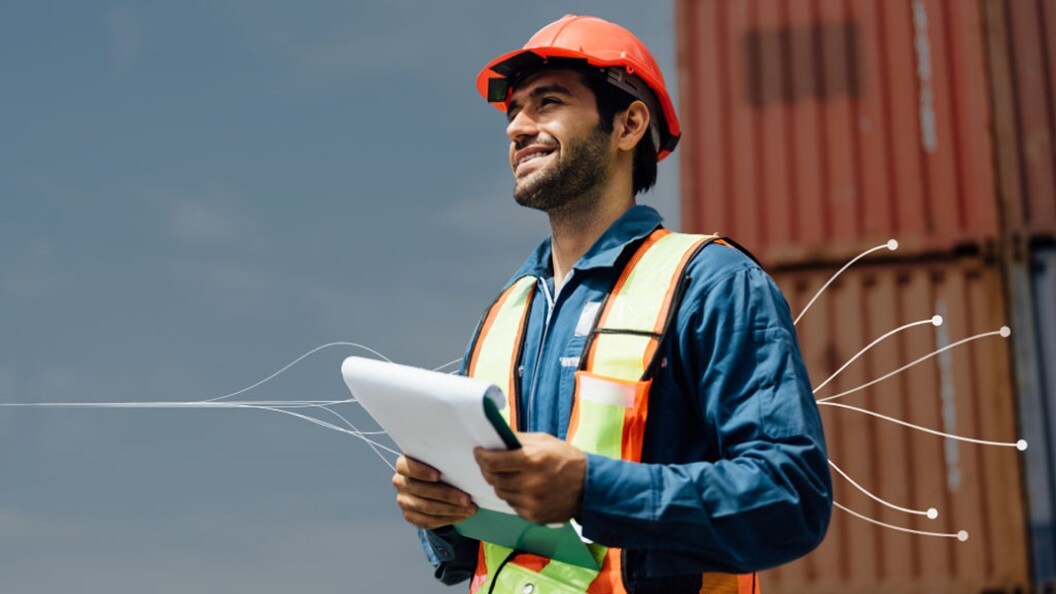Smiling logistics worker holding documents at a container yard.