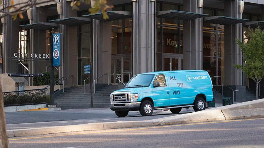 A Maersk delivery van is parked outside a modern urban building, showcasing the brand’s “All The Way” slogan.