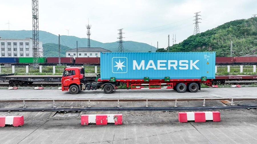 Red truck hauling a Maersk container at a rail terminal.