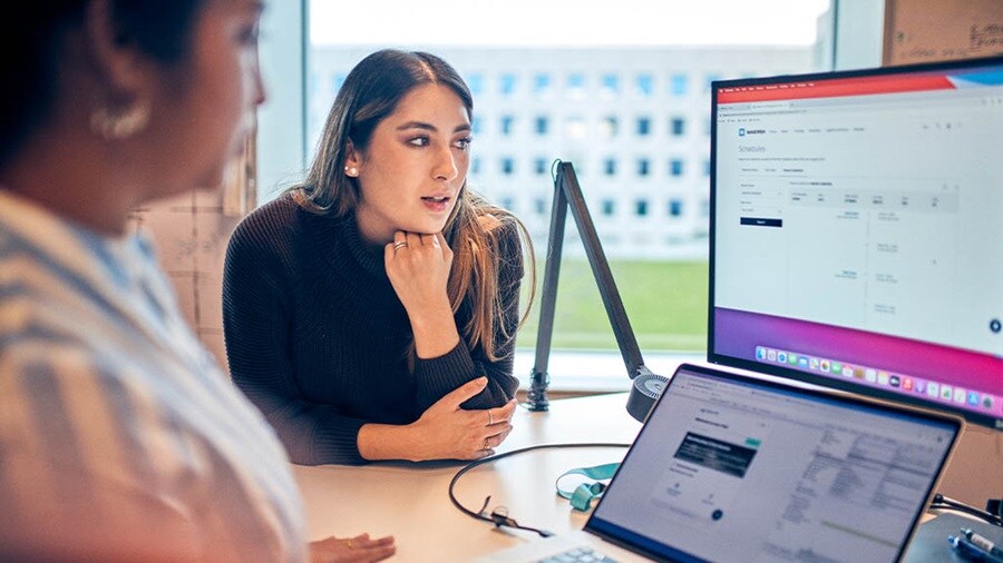 Two professionals are discussing shipping schedules on a computer screen in a modern office.