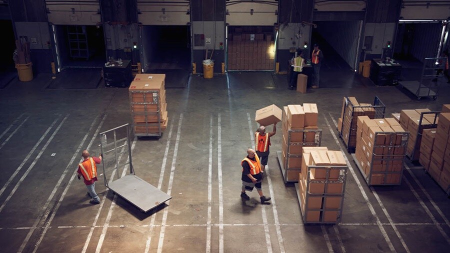 Warehouse workers in high visibility vests organize and load packages onto trucks in a large, industrial distribution center