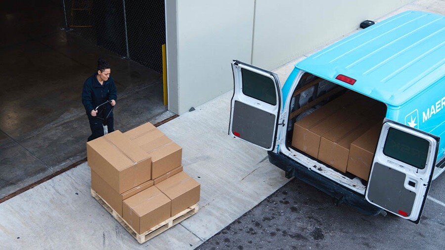 A logistics worker prepares to load a Maersk delivery van with cardboard boxes.