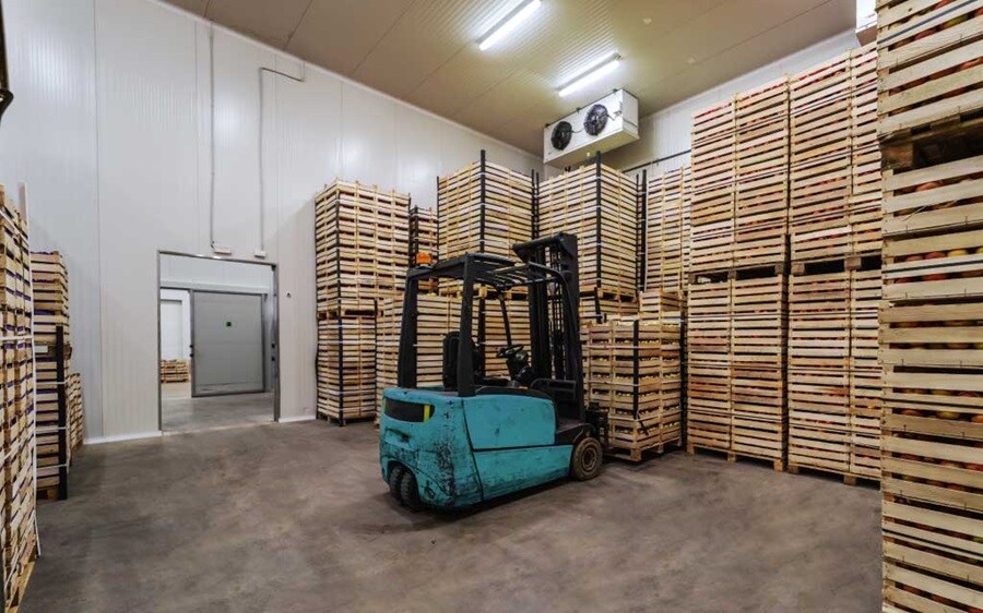 Forklift in cold storage warehouse with stacked crates.
